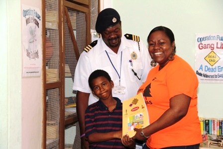 Manager of Caribbean Cable Communications Mrs. Trecia Daniel, officially handing over the books to one of the children at the Creative Youth Academy at the old Cotton Ground Police Station on December 23, 2014 while volunteer at Creative Youth Academy Mr. Joseph Williams looks on